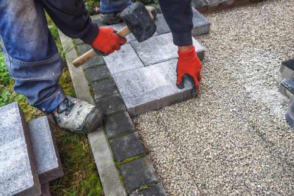 hand with rubber hammer install paving block